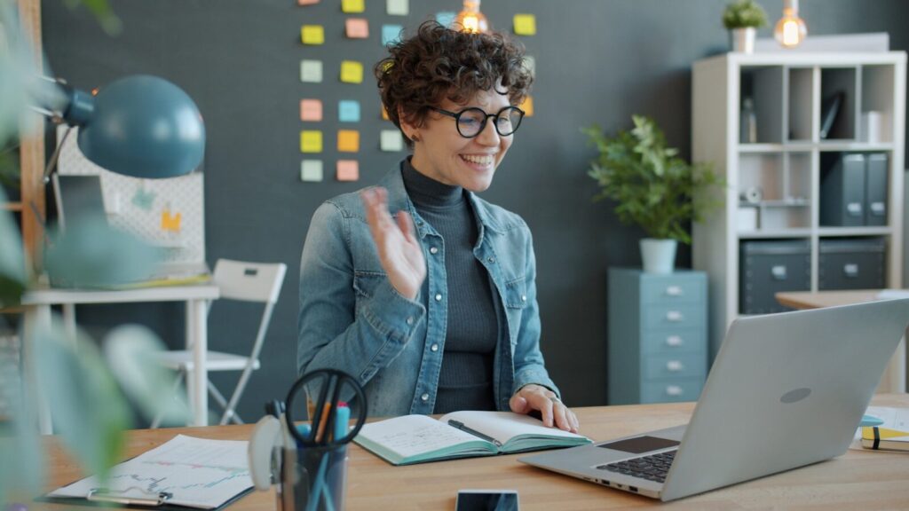 Woman waving hello during a video call at desk